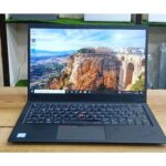Matte black Lenovo ThinkPad X1 Carbon laptop open on an executive desk showing the iconic red TrackPoint.